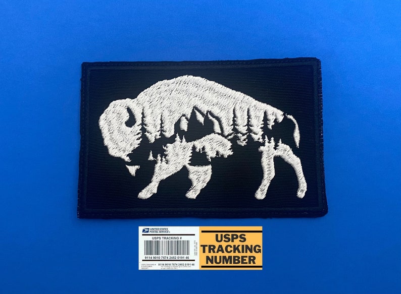 May include: White embroidered patch with a silhouette of a buffalo with a forest inside. The patch is on a black background. The text "USPS TRACKING NUMBER" is on a yellow label below the patch.