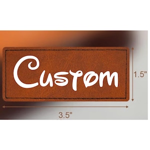 May include: A rectangular brown leather patch featuring the white text Custom in a stylized font. The patch has black stitched borders and is shown with dimension lines indicating a height of 1.5 inches and a width of 3.5 inches.