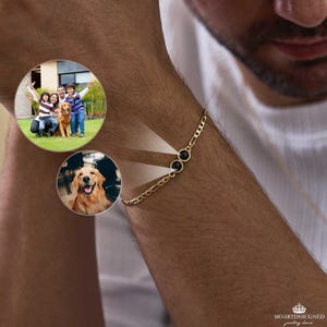 Könnte beinhalten: Ein goldenes Armband mit zwei schwarzen, kreisförmigen Steinen. Das Armband befindet sich an einem Arm. Die Kette hat ein filigranes Design. Das Bild zeigt auch eine Familie und einen Hund.