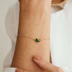May include: A gold chain bracelet with two green gemstone accents. The gemstones are pear-shaped and have a slight yellow hue.