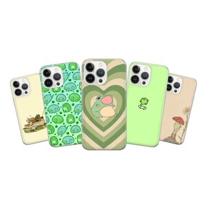 May include: Five different iPhone cases with green and white designs featuring frogs, mushrooms, and hearts. The cases are all clear and show the phone's camera lenses.
