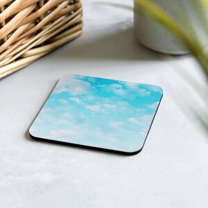 Puede incluir: Posavasos cuadrado con diseño de cielo y nubes. El posavasos tiene un borde negro y un acabado brillante. La imagen muestra un cielo azul brillante con nubes blancas esponjosas, creando una estética alegre y aireada. Este posavasos es perfecto para cualquier espacio.
