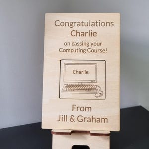 May include: A rectangular light-coloured wooden plaque resting on a matching wooden stand. The plaque is engraved with the text: Congratulations Charlie on passing your Computing Course! From Jill & Graham, featuring a graphic of a computer.