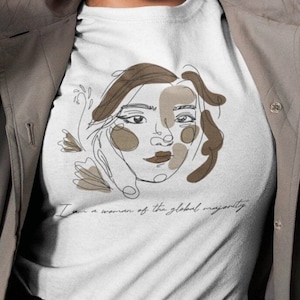 Könnte beinhalten: Weißes T-Shirt mit einer braunen Linienzeichnung eines Frauen Gesichts und dem Text "Ich bin eine Frau der globalen Mehrheit".