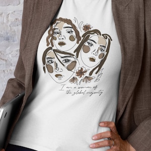Könnte beinhalten: Weißes T-Shirt mit einer Grafik aus drei braunen Linienzeichnungen von Frauen mit Blumen. Der Text "Ich bin eine Frau der globalen Mehrheit" ist unter der Grafik gedruckt.
