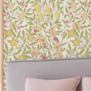 以下が含まれることがあります： 金色のデスクランプ、明るい灰色のヘッドボード、ピンクのクッションを備えた寝室のシーン。 壁紙は、クリーム色の背景に、黄色とピンクの果物と緑の葉が繰り返されるパターンになっています。