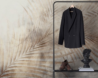 Könnte beinhalten: Ein schwarzer, zweireihiger Blazer hängt an einer schwarzen Kleiderstange. Darunter liegen braune Lederschuhe und eine schwarze Büstenskulptur auf einem Regal. Der Hintergrund zeigt ein beiges und braunes Palmenblattmuster.