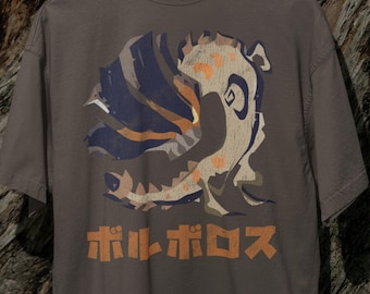 May include: A gray t-shirt featuring a stylized illustration of a creature with orange, blue, and beige accents. The Japanese text "ボルボロス" is printed in orange below the illustration. The shirt is hanging on a wooden hanger.