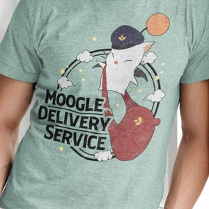 May include: A light green t-shirt featuring a cartoon character with the text "MOOGLE DELIVERY SERVICE". The character is white with a red pouch, a black hat, and a yellow orb. The design is encircled by a black ring with clouds and stars.