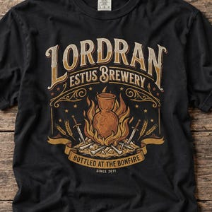 Puede incluir: Una camiseta negra de manga corta con un estampado gráfico que incluye el texto "LORDRAN ESTUS BREWERY BOTTLED AT THE BONFIRE SINCE 2011". El diseño muestra un frasco central rodeado de llamas, espadas cruzadas y espigas de trigo en tonos naranja y beige.