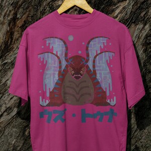 May include: Pink t-shirt with a graphic print of a creature with wings and the text "カス・トワ" in Japanese.