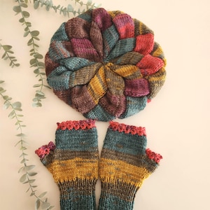 May include: A knitted hat and fingerless gloves set in a variety of colours. The hat features teal, yellow, purple, and red. The fingerless gloves have a teal base with yellow and brown stripes, and a red scalloped trim.