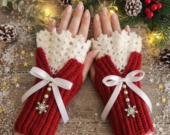 May include: A pair of fingerless gloves featuring a deep red ribbed knit base and a cream-colored crocheted lace cuff. Each glove is adorned with a white satin ribbon bow, a string of small faux pearls, and a silver-toned snowflake charm.