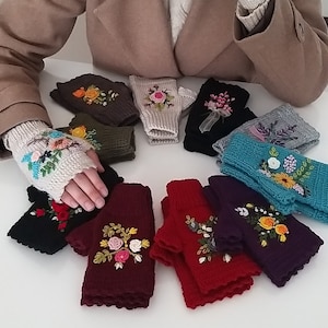May include: A collection of 10 pairs of fingerless gloves with floral embroidery. The gloves are in various colors, including black, red, purple, teal, and white. Each pair features a different floral design.
