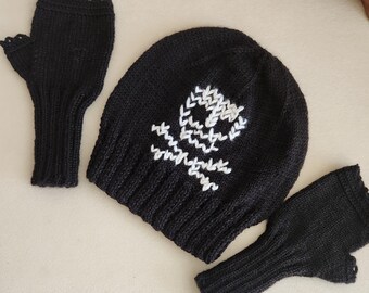 May include: A black knit beanie and fingerless gloves set. The beanie features a white skull and crossbones design. The gloves and beanie are made of a soft, textured knit material. The set is displayed on a neutral background.