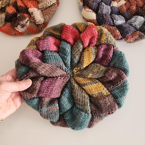 May include: A colorful knitted round coaster with a spiral pattern in shades of red, pink, purple, teal, brown, and yellow.