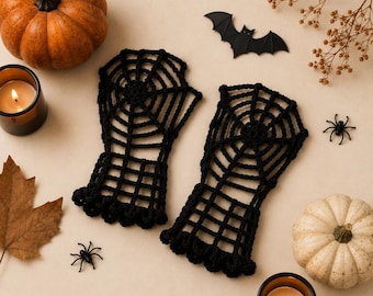 May include: A pair of black fingerless gloves featuring a crocheted spiderweb pattern. The gloves have a scalloped edge at the wrist and are displayed alongside two pumpkins, two lit candles, a black bat cutout, and two small spiders.