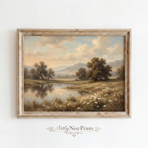May include: A framed landscape painting shows a tranquil waterscape with trees, grassy banks, and distant hills under a cloudy sky. The artwork is in a rustic, light-toned wooden frame, giving a vintage feel. The painting is signed "Artly Nest Prints".