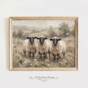 May include: A framed print featuring three sheep with black faces and fluffy white wool, standing in a field of tall grass and wildflowers. The artwork has a muted color palette with a vintage aesthetic. The frame is a light wood color.