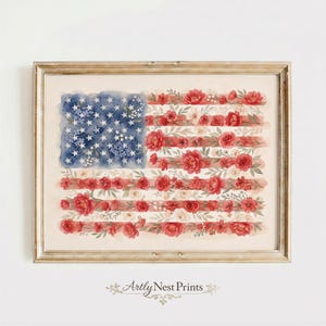 Op de afbeelding: Een ingelijste aquarelprint van de Amerikaanse vlag, waarbij de sterren en strepen zijn vervangen door bloemen. Het blauwe veld heeft witte sterren en blauwe bloemen. Rode en witte bloemen vormen de strepen. De print zit in een goudkleurige lijst.