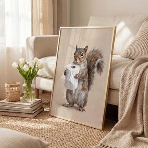 May include: Framed artwork featuring a detailed painting of a squirrel holding a roll of toilet paper. The squirrel is depicted in shades of gray and brown, set against a neutral background. The artwork is framed in a gold-colored frame, suitable for home decor.