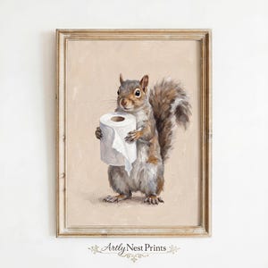 May include: A framed print featuring a detailed painting of a squirrel holding a roll of toilet paper. The squirrel is depicted in shades of gray and brown, with a fluffy tail. The background is a soft beige, and the frame is a light brown.