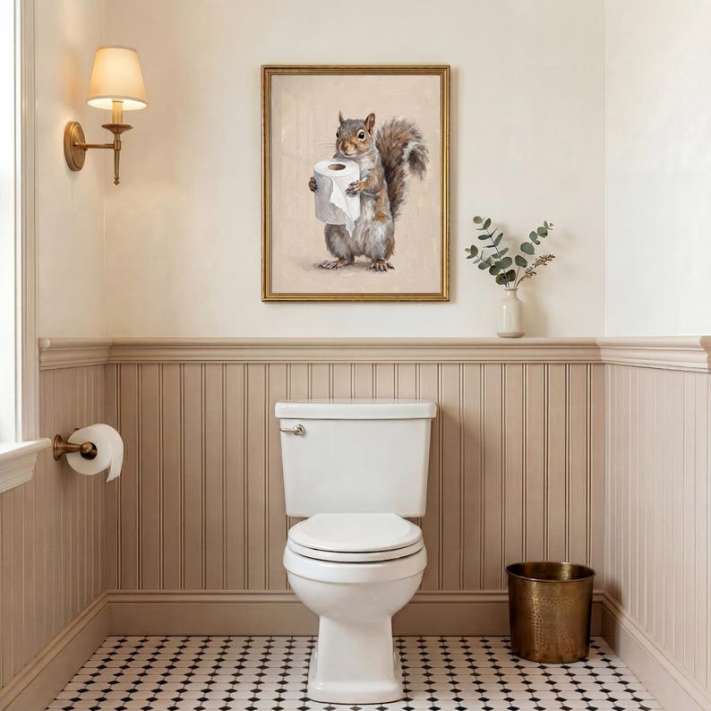 May include: A bathroom scene featuring a white toilet, a gold-framed squirrel art print holding toilet paper, and a brass wastebasket. The walls are painted in neutral tones with a black and white tiled floor. A wall sconce provides soft lighting.