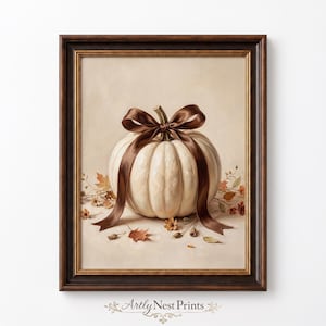 May include: A framed wall art print featuring a white pumpkin tied with a dark brown satin ribbon. The pumpkin sits on a light beige surface surrounded by scattered autumn leaves and small flowers. The frame is dark brown with gold trim.