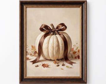 Puede incluir: Una lámina de arte enmarcada que muestra una calabaza blanca atada con una cinta de satén marrón oscuro. La calabaza descansa sobre una superficie de color beige claro rodeada de hojas de otoño y pequeñas flores. El marco es marrón oscuro con borde dorado.