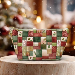 May include: A rectangular cosmetic bag with a patchwork design in shades of red, green, and beige. The bag features a gold zipper and is decorated with holly and berry motifs, perfect for holiday gifting.