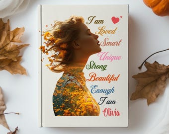 May include: A book cover featuring a woman's profile with a floral overlay. The text includes "I am Loved, Smart, Unique, Strong, Beautiful, Enough, I am Olivia." The cover is surrounded by autumn leaves and a pumpkin.