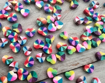 Könnte beinhalten: Eine Sammlung bunter herzförmiger Perlen mit einem wirbelnden Regenbogenmuster. Die Perlen sind aus Polymer Clay gefertigt und perfekt für die Schmuckherstellung oder zum Basteln.