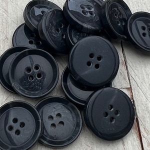 Könnte beinhalten: Eine Gruppe von 10 schwarzen Kunststoffknöpfen mit jeweils vier Löchern. Die Knöpfe sind rund und haben eine glänzende Oberfläche.