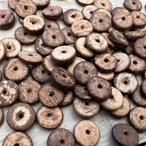 Könnte beinhalten: Ein Haufen brauner und weißer Kokosnussschalenperlen mit einem Loch in der Mitte jeder Perle.