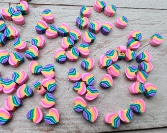 Könnte beinhalten: Eine Sammlung bunter herzförmiger Perlen mit einem Regenbogen-Swirl-Muster. Die Perlen sind aus Polymer Clay gefertigt und haben ein Loch in der Mitte zum Auf fädeln.