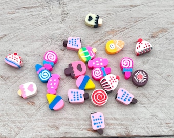 Könnte beinhalten: Eine Sammlung bunter, kleiner, plastischer Charms zum Thema Süßwaren. Die Charms sind in Form von Eiswaffeln, Cupcakes, Lutschern und anderen süßen Leckereien gestaltet.