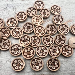 Könnte beinhalten: Eine Sammlung hellbrauner Holzknöpfe mit einem floralen Design, das in die Oberfläche geschnitzt ist. Die Knöpfe sind rund und haben zwei Löcher zum Annähen. Das florale Design ist dunkelbraun.