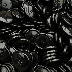 Könnte beinhalten: Ein großer Haufen schwarzer Plastikknöpfe mit jeweils vier Löchern. Die Knöpfe sind glänzend und haben eine glatte Oberfläche.