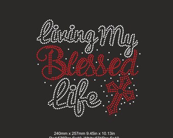 Pode incluir: Modelo de strass para uma camiseta ou outra peça de roupa. O design apresenta o texto "Living My Blessed Life" com uma cruz em strass vermelho e branco. O design mede 240 mm por 257 mm.