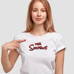 May include: A white short-sleeved t-shirt featuring the red and black text logo for The Simpsons printed on the center of the chest. The garment has a round neckline and cuffed sleeves, providing a clean and simple look for casual wear.