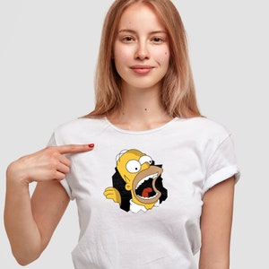 Op de afbeelding: Een wit T-shirt met korte mouwen en een grafische print van het stripfiguur Homer Simpson. Het personage is afgebeeld met een wijd open mond en lijkt uit een grillig zwart gat in de stof van het witte T-shirt tevoorschijn te komen.
