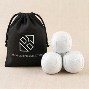 Może przedstawiać: Czarny worek ze sznurkiem z białym napisem PREMIUM BALL COLLECTION i geometrycznym logo, w towarzystwie trzech białych kulistych piłek z tym samym wytłoczonym geometrycznym logo na ich powierzchniach, ułożonych w małą grupę.