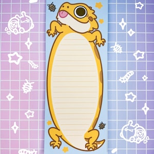 May include: A blue notepad featuring a yellow bearded dragon illustration. The dragon is facing the left side of the notepad and has its tongue sticking out. The notepad has a lined section for writing notes. The background is a light blue with yellow stars.