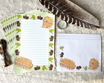 Op de afbeelding: Een set van 10 blanco briefpapierbladen met een groene, bruine en gele rand met een cartoonillustratie van een gesegmenteerd worm. De briefpapierbladen zijn gestreept om op te schrijven.