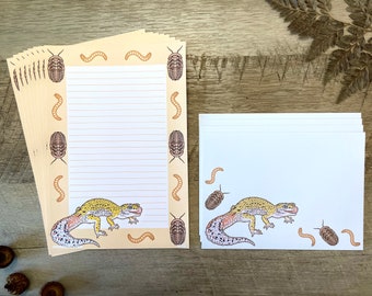 Op de afbeelding: Een set briefpapier met een gele en zwarte gekko met bruine wormen en kevers op een beige achtergrond. Het briefpapier bevat gestreept schrijfpapier en enveloppen.