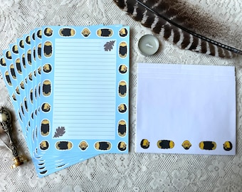 Op de afbeelding: Een set blauw briefpapier met een rand van geïllustreerde gele en zwarte duizendpoten. Het briefpapier is gevouwen en gestapeld op een wit oppervlak. Een witte envelop met een rand van geïllustreerde gele en zwarte duizendpoten ligt naast het briefpapier.