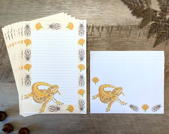 Op de afbeelding: Een set van 10 gele en witte briefkaarten met een baardagame en insecten op de rand. De bijpassende enveloppen zijn wit met een baardagame en insecten.