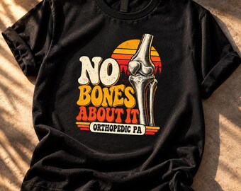 May include: A black short-sleeve t-shirt featuring a graphic of a human knee joint and the text NO BONES ABOUT IT ORTHOPEDIC PA. The design includes a sunset background with orange, yellow, and red horizontal stripes behind the anatomical illustration.
