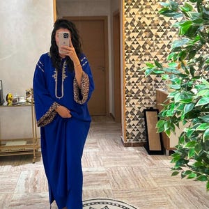 Puede incluir: Un vestido azul real de manga larga con ribete de estampado de leopardo en las mangas y un diseño de cuentas en la parte delantera.
