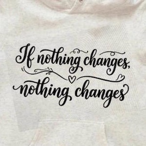 May include: A pale grey hoodie with a front pocket and a drawstring hood. The hoodie displays the text "If nothing changes, nothing changes" in black script across the front.